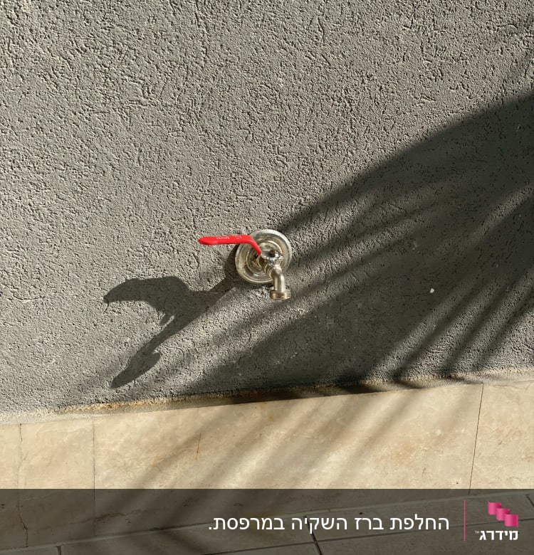 ברז מים עם ידית אדומה על קיר אפור